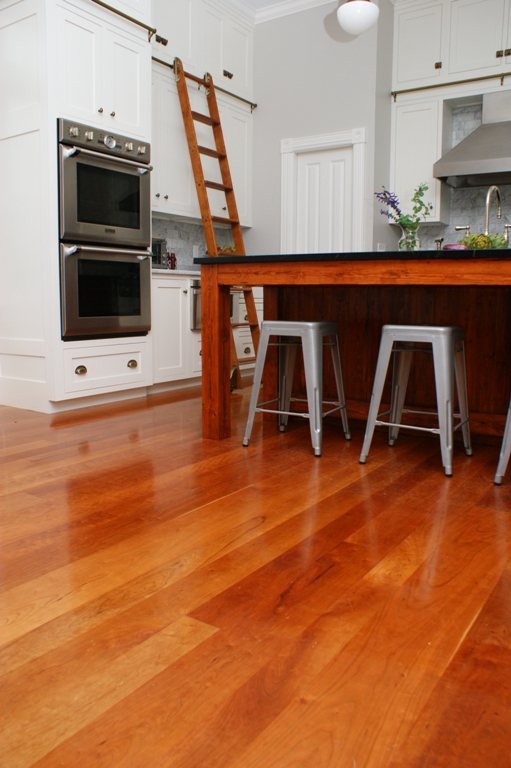 Warm colored cherry wood floors brighten an all white kitchen.